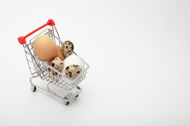 Different color and size eggs are in the grocery cart on the white background