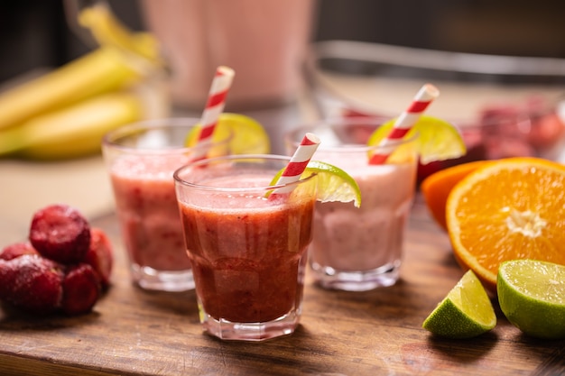 Different colors of red and pink smoothies in cups with paper straws on a kitchen table.