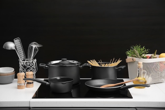 Photo different cooking utensils on electric stove against black background