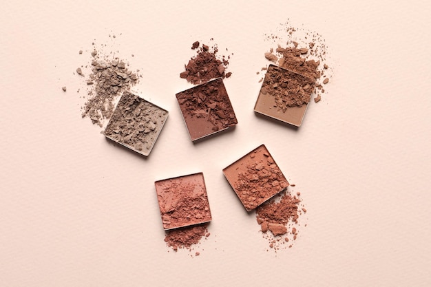 Different crushed eye shadows on beige background flat lay