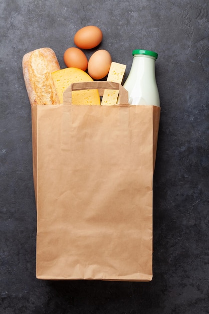 Different dairy food eggs and baguette in recycling paper bag on stone table Eco food concept