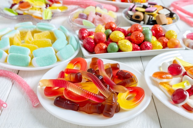 Different delicious colorful gummy candies on plates Vertical view