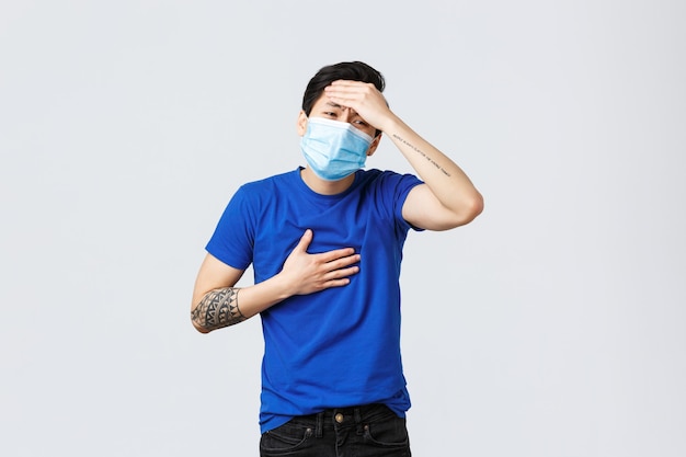 Different emotions, social distancing, self-quarantine on coronavirus and lifestyle concept. Asian man feel sick and ill, catching flu or covid-19, wear medical mask, having fever and pain in lungs.