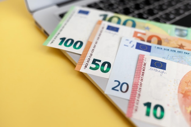 Different euro bills on a laptop background and on a yellow\
background