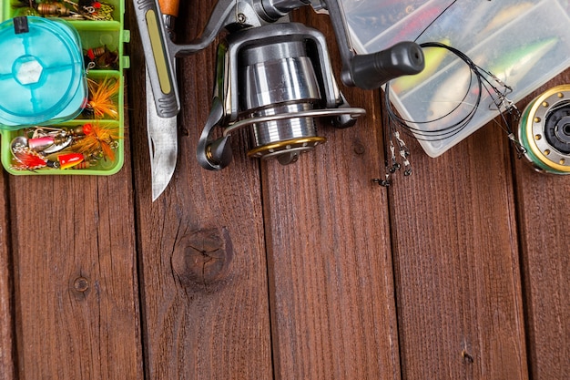 Different fishing tacles with lures and reels on wooden brown background with place for text. Design for advertisment and publishing.