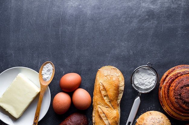 Different fresh, crisp bakery products and baking ingredients on black chalkboard background. Copy space for recipe and text