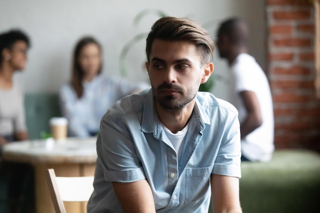 Photo different friends sitting in cafe after study spending time together focus on frustrated lonely shy guy sitting apart separately of others teenagers feels unhappy having problems with communication