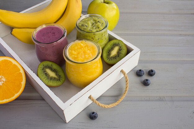 Different fruit smoothies or puree in the small glass jars on the white tray on the grey wooden