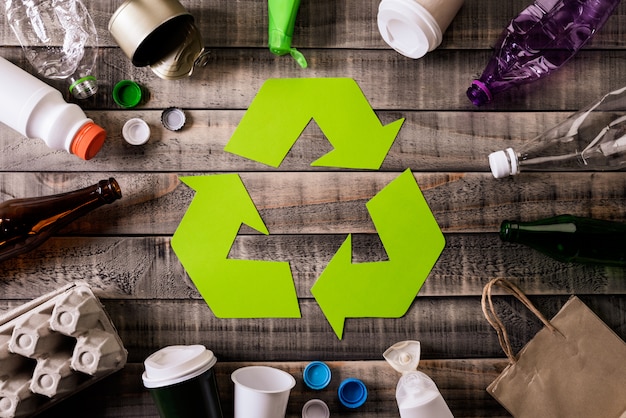 Different garbage materials with recycling symbol on table background.