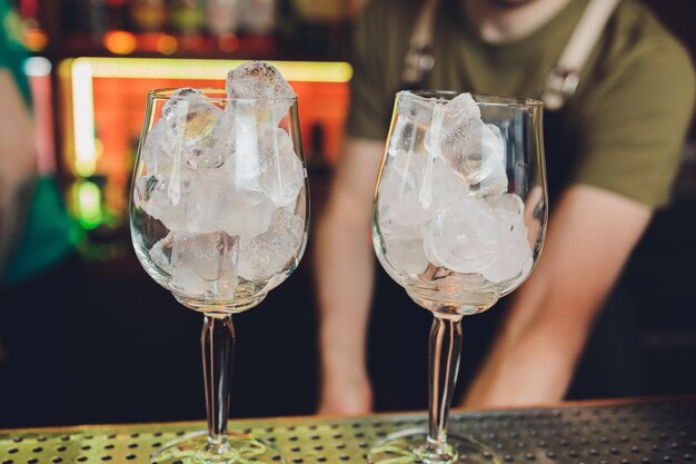 Different glasses and metal jigger and measuring cup are stands on the bar counter Blurred bartender in background