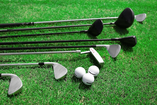 Different golf clubs in a row and balls on a green grass