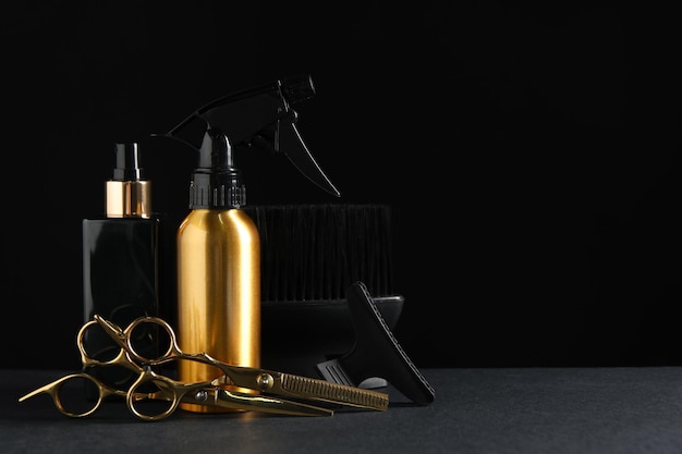 Different hairdresser tools on grey table against black background Space for text