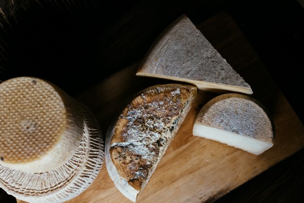 Different homemade cheeses on a dark wooden table. Pieces and cheese heads of Gorgonzola, Asiago, Maasdam, Gauda, Paramezan and Edam. Top view.