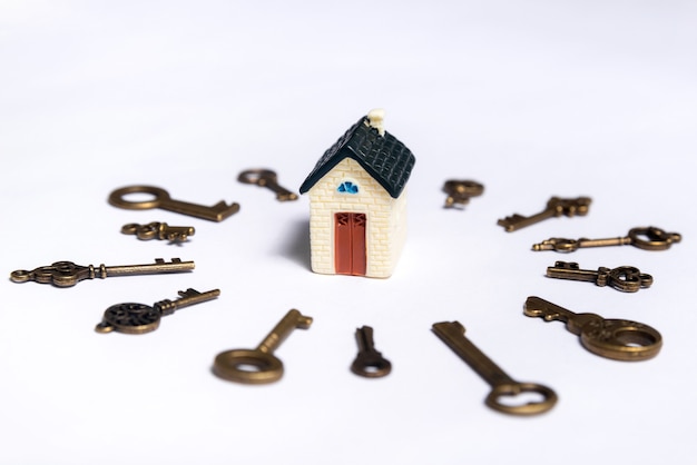 Different keys and a little house on a white background, concept of real estate