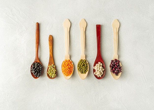 Different kinds of beans in spoons on white background