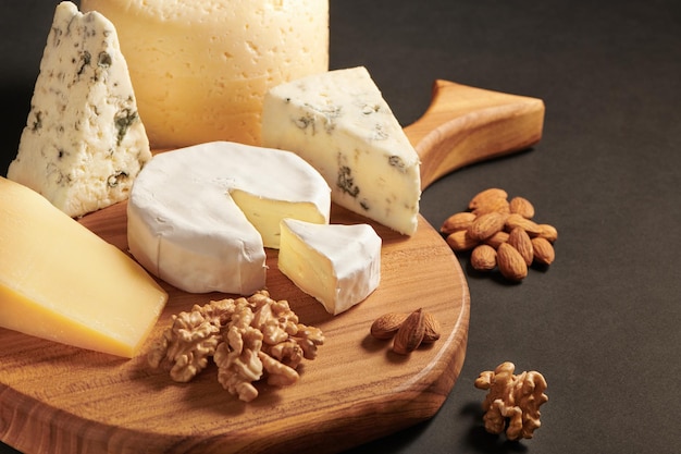 Different kinds of delicious cheese on wooden cutting board. Still-life. Set of cheeses le brie, dor blu, parmesan. Black background with copy space