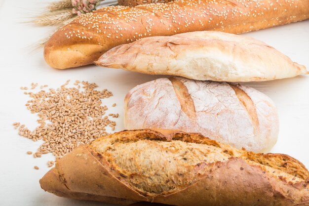 Different kinds of fresh baked bread on a white wooden background. side view.