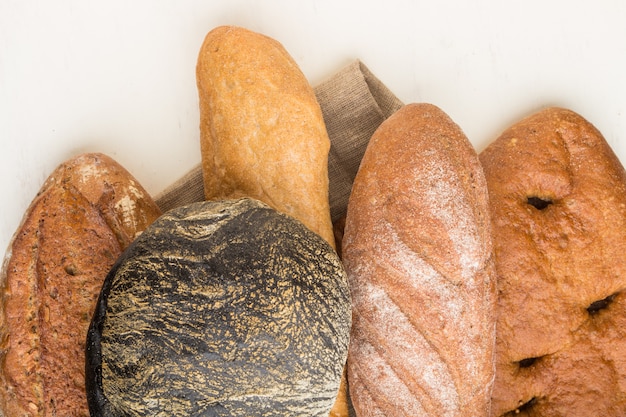 Different kinds of fresh baked bread on a white wooden background. top view, close up.