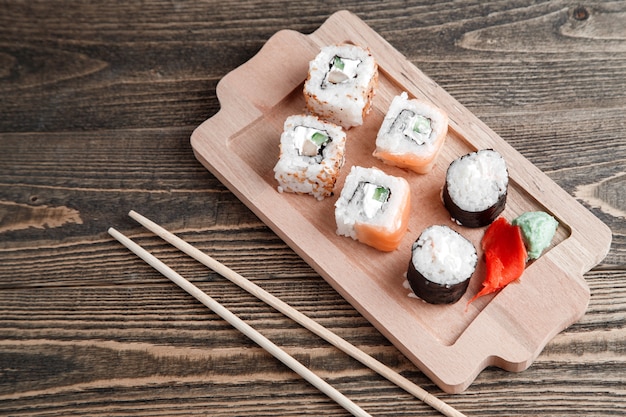 different kinds of Japanese rolls with wasabi and ginger on bamboo tray on wood