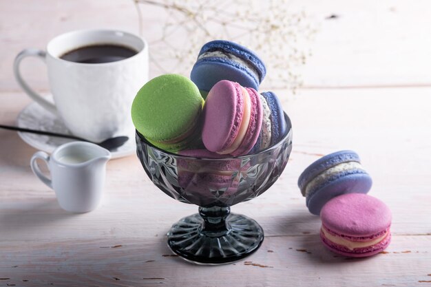 Different kinds of macaroons in glass vase on light wooden background