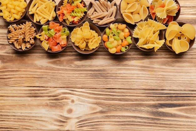 Different kinds of pasta in bowls on wooden surface