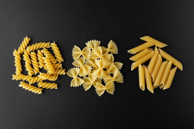 Different kinds of raw pasta with copy space on black background