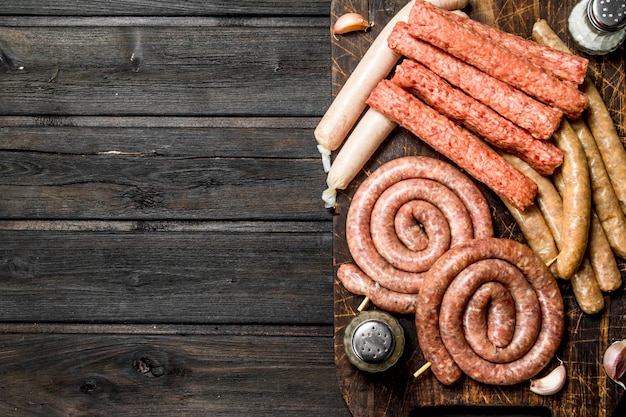 different kinds of raw sausages on wooden board with spices