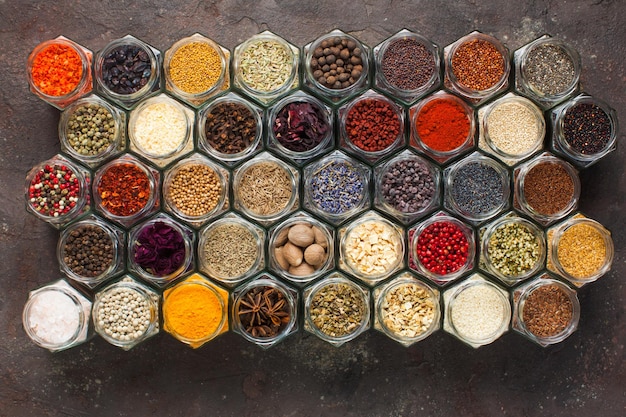 Different kinds of spices and herbs in glass on grey background, top view