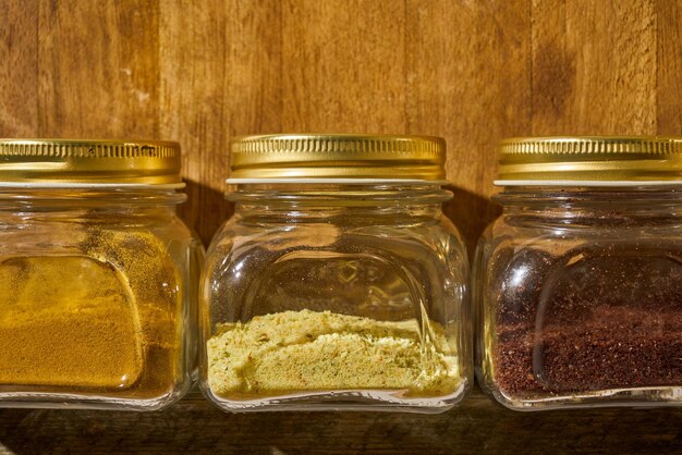 Different kinds of spices in vintage jars on a wooden kitchen shelf.