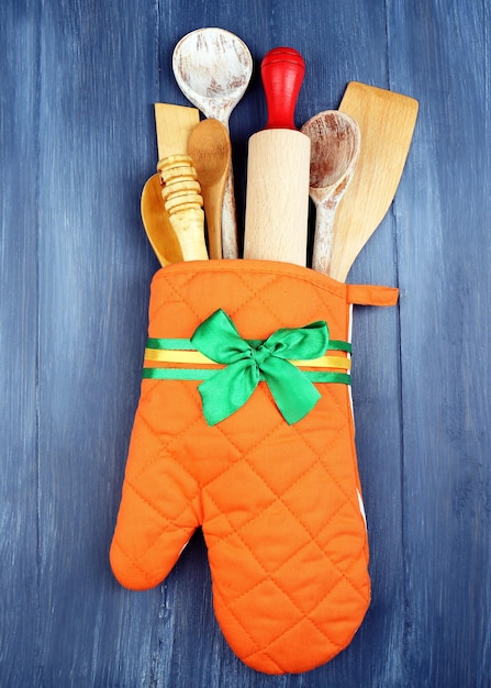 Different kitchen utensils in potholder on wooden background