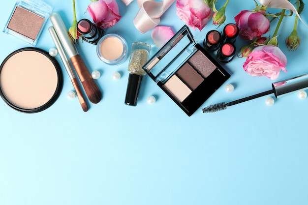 Different makeup cosmetics and flowers on blue background