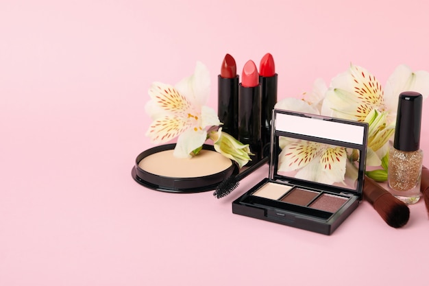 Different makeup cosmetics and flowers on pink background