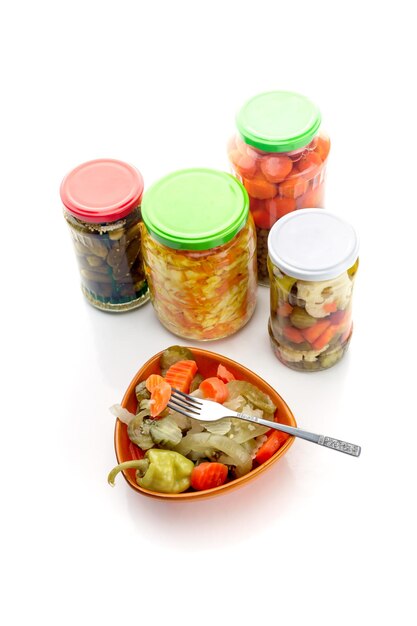 Different marinated vegetables in a bowl and jars on a white background closeupxA