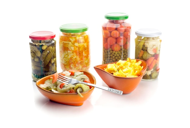 Different marinated vegetables in cans and bowls on white background closeup