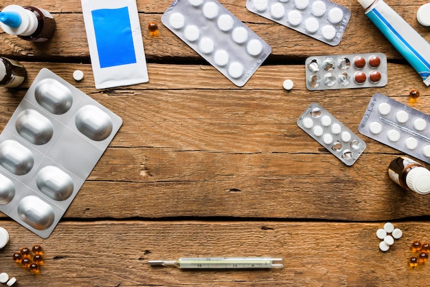 Different medical pills, antibiotics, nasal drops, a thermometer on a wooden background