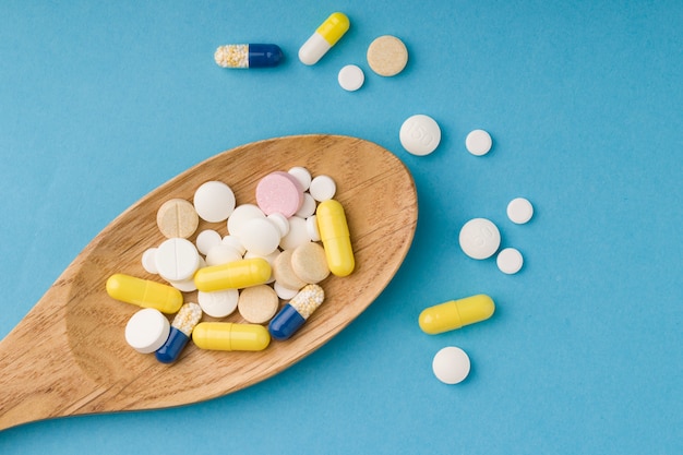 Different medicine pills, tablets and capsules on wooden spoon.