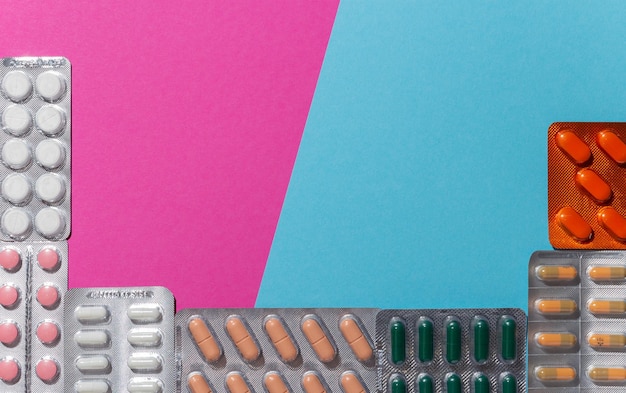 Different medicines: tablets, pills in blister pack, medications drugs on blue and pink background.