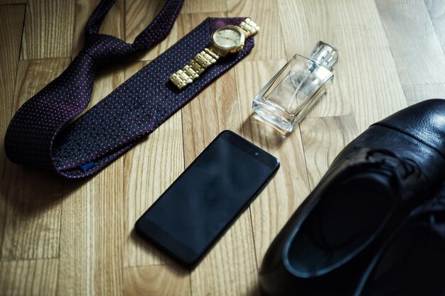 Different men's accessories such as shoes tie watches parfum and telephone are on the wooden background