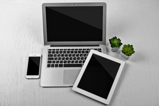 different modern devices with green plants on light table