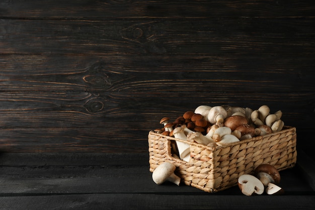 Different mushrooms in basket on wooden, space for text