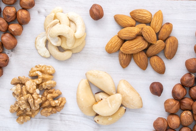 Different nuts piles on wooden table. Nuts background. Hazlenuts, walnuts, almond, brazilian and cashew nuts.