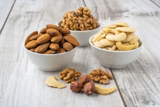 Different nuts in the white bowl on lignt wood table. Almond seeds, walnuts and cashew nuts.