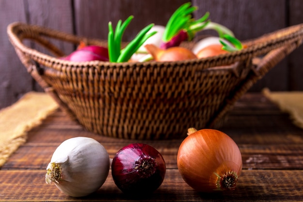 Different onions in basket on wooden background. Rustic style.  Red, white and golden.