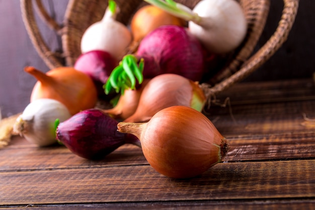 Different onions in basket on wooden . Rustic style.  Red, white and golden.