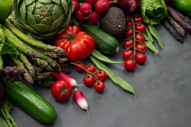 Different organic vegetables - asparagus, tomatoes cherry, avocado, artichoke, pepper, lime, lemon, salt on gray background. Food fame with copy space, top view. Raw vegan vegetarian concept