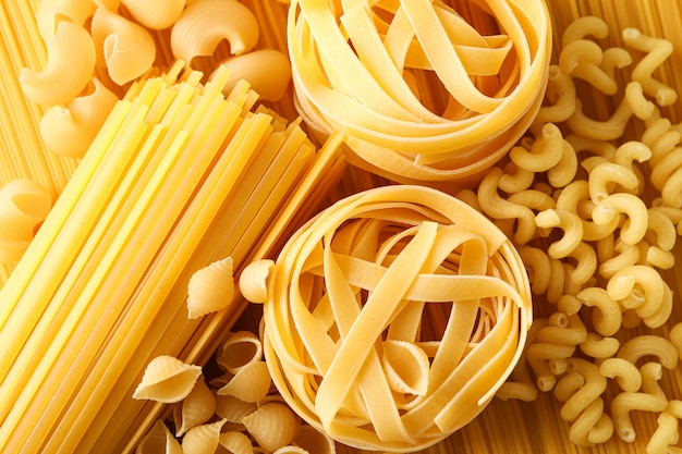 Different pasta as background, closeup. Dry uncooked whole pasta