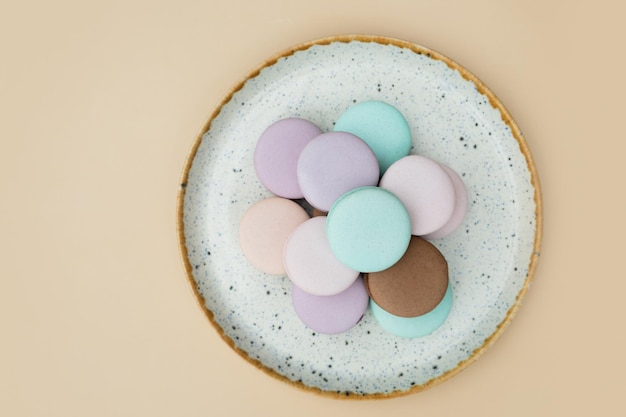 Different pastel colors pastry macarons in round plate top view on a beige background