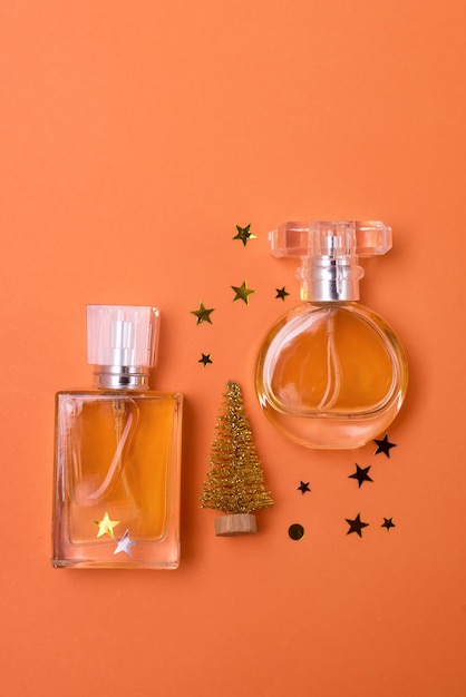 Different Perfume Bottles with Golden Christmas Tree and Golden Confetti on Orange Background