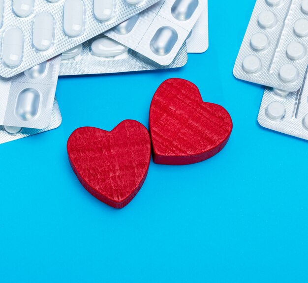 Разные таблетки в упаковке и два красных сердечка