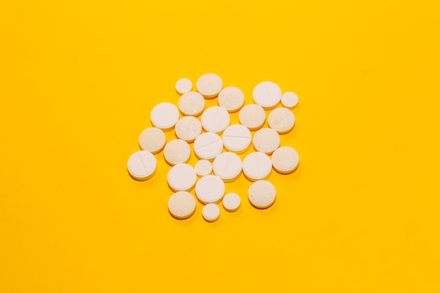 Different pills and vitamins are scattered on a yellow background. space for text, closeup